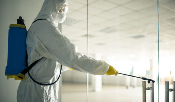 Sanitary worker sprays an empty business center with antiseptical liquid to prevent covid-19 spread. A man wearing disinfection suit cleaning up the shopping mall. Nobody, health, isolated concept.